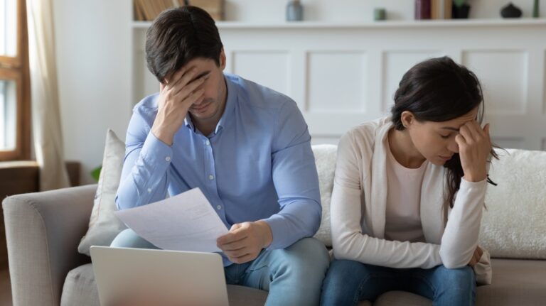 Couple sitting on a couch dejected over paperwork