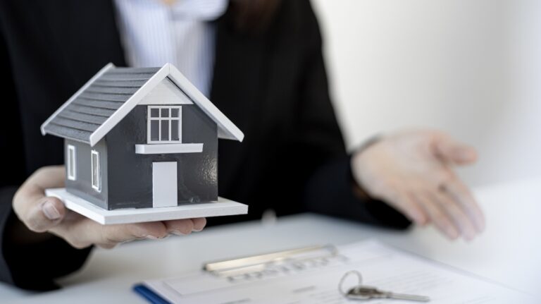 Woman holding a model house in her hand over paperwork